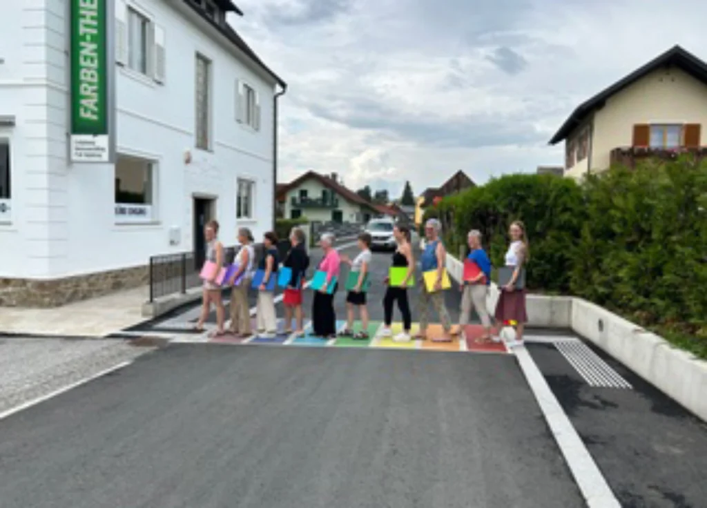 10 Personen die mit bunten Mappen unter den Armen über einen Regenbogenfarbenen Zebrastreifen gehen