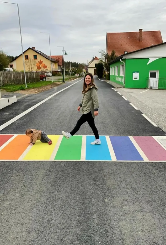 Eine junge Frau die mit einen Baby über einen bunten Zebrastreifen geht